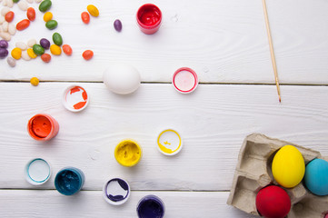 Easter eggs, paint and candy on wooden table