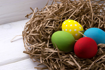 Easter eggs in nest on white wooden background
