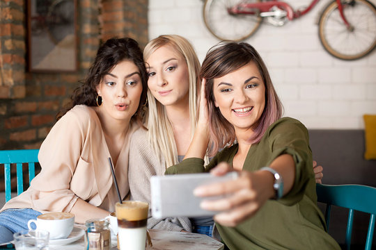 Female Friends In Cafe Taking Selfie Using Smart Phone. Drinking coffee, having fun and enjoying their time.