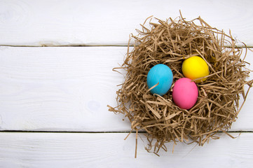 Holiday colored easter eggs in nest on white wooden table top view