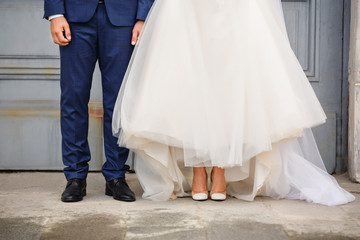 Wedding fashion. Groom in blue suit and bride in white wedding dress and shoes on high heels. Marriage couple