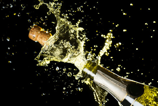 Close up image of champagne cork flying out of champagne bottle. Celebration theme with explosion of splashing champagne sparkling wine on black background.