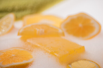 yellow lemon glycerine soap in bubbles with fresh slices of lemon and orange