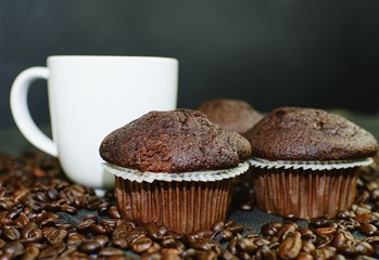 Dark muffins, cups of coffee and coffee beans on black background. 