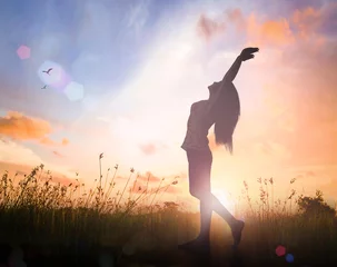 Foto op Canvas Freedom concept: Silhouette of healthy woman raised hands for praise and worship God at autumn sunset meadow background © Choat