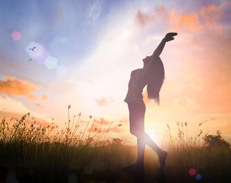 Freedom concept: Silhouette of healthy woman raised hands for praise and worship God at autumn sunset meadow background