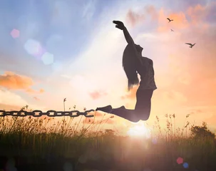 Muurstickers Freedom concept: Silhouette of a woman jumping and broken chains at orange meadow autumn sunset  with her hands raised © Choat