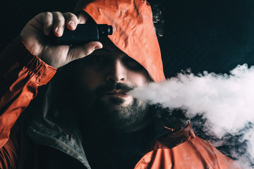 Man smoker vaping e-cigarette with e-liquid from vape RDA device, breathes out vapor and looks at...
