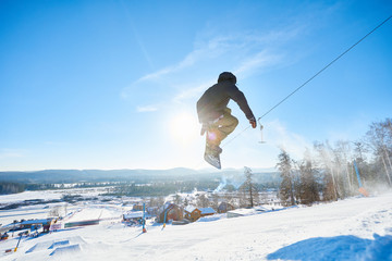 Naklejka na ściany i meble Full length action shot of young man performing snowboarding stunt jumping high in sunlight at ski resort, copy space