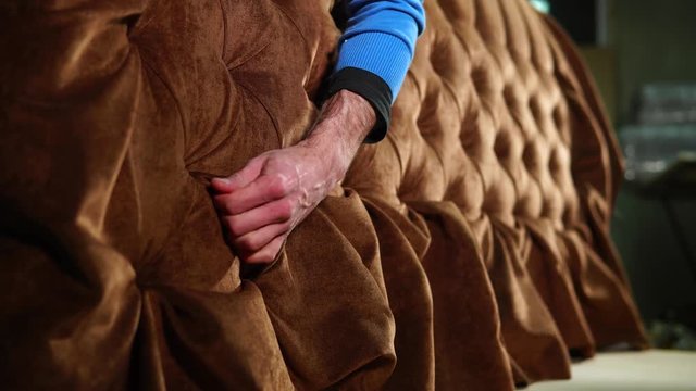 Worker is correcting folds in upholstery of the sofa. Exclusive soft furniture, producing for order in a craft workshop
