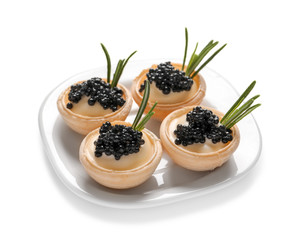 Plate of delicious canapes with black caviar on white background