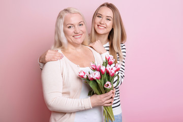 Young daughter and mother with bouquet of flowers on color background