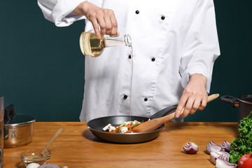Female chef in uniform adding oil to tasty dish on table, closeup