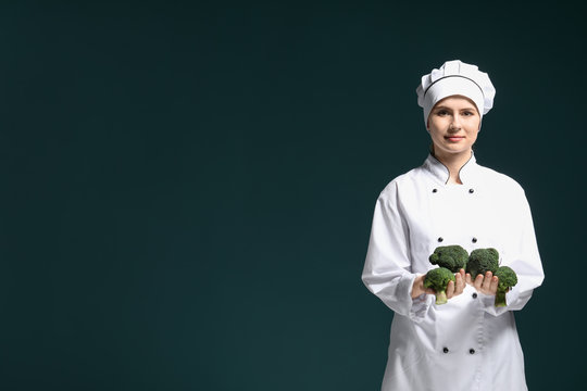 Female chef in uniform with broccoli on dark background