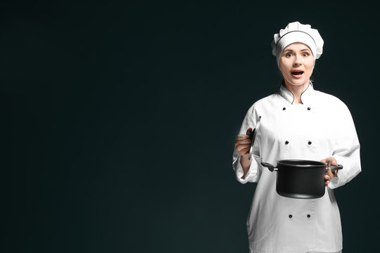 Female chef in uniform with saucepan on dark background