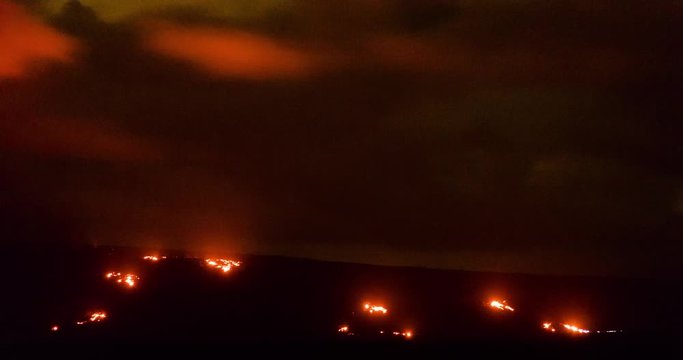 timelapse footage of the lava fields of volcano national park showing the red and orange glow against the night sky and clouds