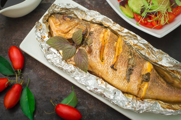 Fried fish with fresh tomatoes, herbs and lemon. Old black background. Top View