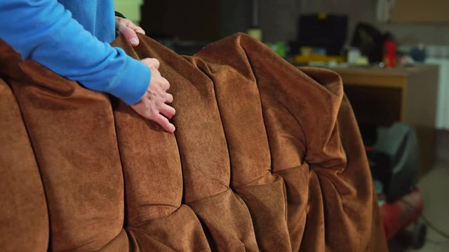 Skilled workman is making a luxury sofa. He is wrapping a base by velvet cloth and creating a design of hand made furniture