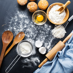 Baking ingredients. Bowl, eggs, flour, eggbeater, rolling pin and eggshells on black chalkboard from above.