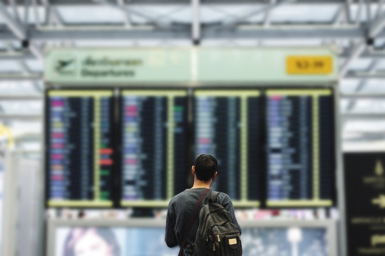 A Man With Backpack Looking On Departure Flight Information Board, For Travel, Go Back Home And Holiday Trip