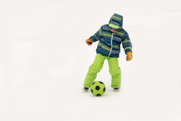 A young lady in a blue ski suit plays football with children in the snow. Yellow sled, sunglasses, bright clothes. Girl happy outdoors. Fun winter vacation for the whole family. Green soccer ball