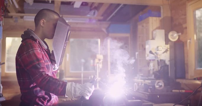 Beautiful woman with short hair is welding metal in a workshop