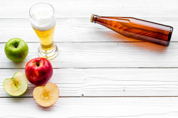 Apple cider poured into glass near bottle and apples. White wooden background top view copy space
