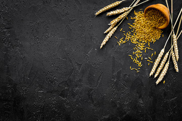 Raw oat in bowl near ears of wheat on black background top view copy space