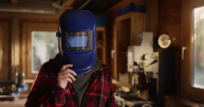 Young attractive woman opens her welding helmet and smiles