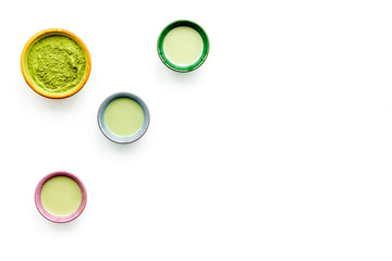 Brew matcha tea. Bowl with powder and cups with beverage on white background top view copy space