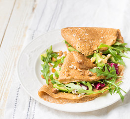 English-style (or Russian-style) useful whole grain pancakes with avocado, radicchio, arugula and almonds on a light wooden background. Useful dietary snack.