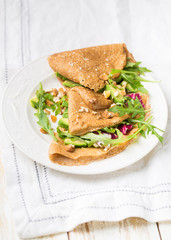 English-style (or Russian-style) useful whole grain pancakes with avocado, radicchio, arugula and almonds on a light wooden background. Useful dietary snack.