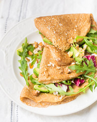English-style (or Russian-style) useful whole grain pancakes with avocado, radicchio, arugula and almonds on a light wooden background. Useful dietary snack.