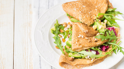 English-style (or Russian-style) useful whole grain pancakes with avocado, radicchio, arugula and almonds on a light wooden background. Useful dietary snack.