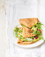 English-style (or Russian-style) useful whole grain pancakes with avocado, radicchio, arugula and almonds on a light wooden background. Useful dietary snack.