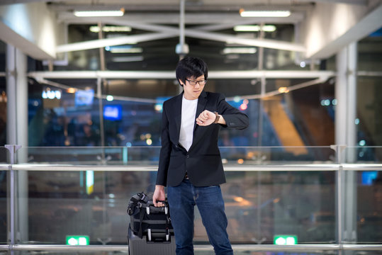 Young asian man checking the time from his watch while waiting for check-in in the international airport terminal, business travel concept