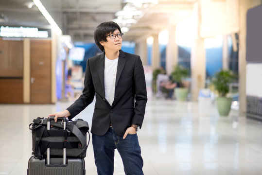Young asian businessman with his suitcase luggage and backpack waiting for airline flight in the international airport terminal, man in business travel concept