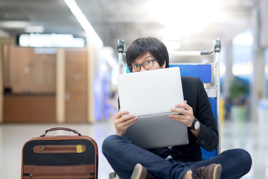 Young asian man posing with laptop computer on airport trolley during waiting for a connecting flight, freelance lifestyle and digital nomad concepts