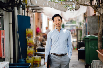 An image of a young and attractive Asian Chinese businessman walking in a street alley. He wears a...