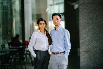 Portrait of two coworkers standing during the day in their office. One is a woman from India, the...