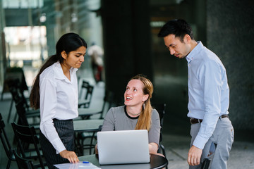 3 people from a diverse team are having a discussion around a laptop computer during the  day in an...