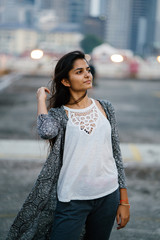 Fototapeta premium Portrait of an attractive Indian woman wearing a casual outfit while smiling and striking her hair glamorousdly in front of the camera. She is standing in a parking lot and enjoying the view.