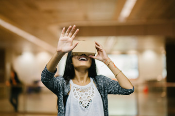 A portrait of a beautiful Indian woman trying out a VR goggles for the first time while standing in the middle of the hallway . She looks amazed and smiling as she looks through the goggles.