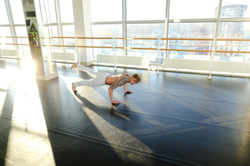 Faculty of physical education student diligently push up, handsome guy in white trousers doing gymnastic exercises. Tattooed male in well-equipped light spacious university hall. Concept of man