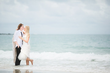 Fototapeta na wymiar bride in wedding dress and groom hugging at the sea. couple love on deserted beach.