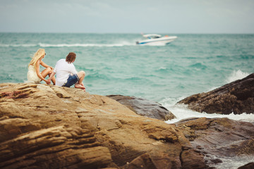 Fototapeta premium couple in love sit on rocky beach. newlyweds looking at the passing boat.