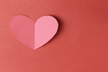 Heart shape of paper on the red cardboard background.