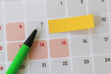 Green pen points to a seven number of calendar and have blank yellow note paper.