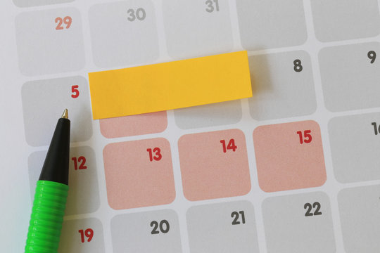 Green pen points to a five number of calendar and have blank yellow note paper.