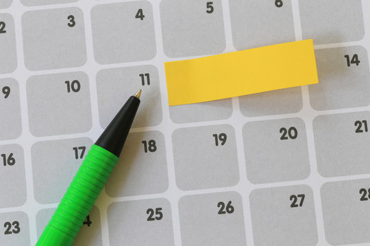 Green pen points to a eleven number of calendar and have blank yellow note paper.